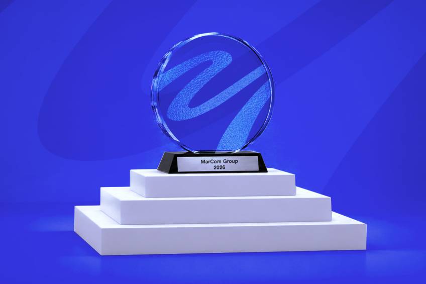 MarCom Group 2026 award trophy displayed on a white podium against a blue branded background.