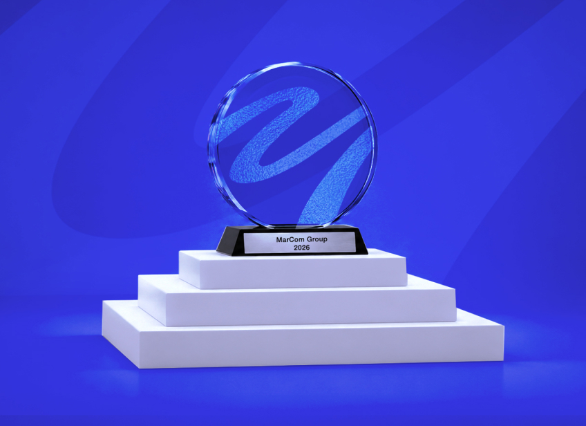MarCom Group 2026 award trophy displayed on a white podium against a blue branded background.