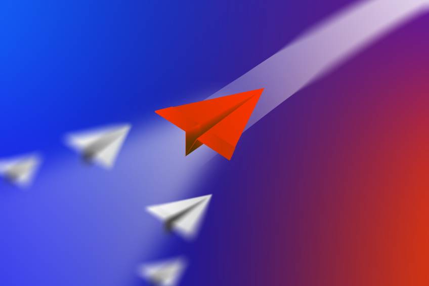 Red paper airplane flying ahead of white paper airplanes on a blue-to-red gradient background.